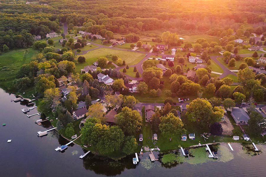 About Our Agency - Aerial View of a Lakefront Community, Sun Setting Over the Trees