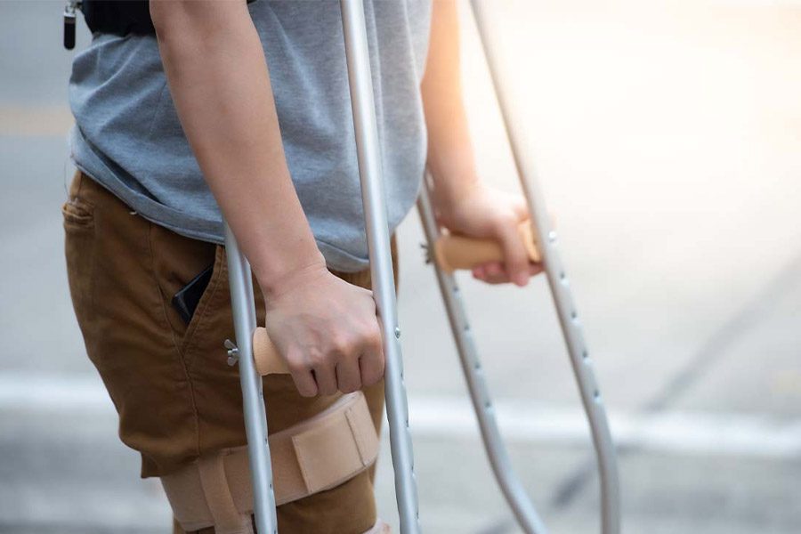 Disability Insurance - Close-up of Woman’s Lower Body and Knee Support Using Crutches Standing and Trying to Walk after Suffering a Work Related Injury