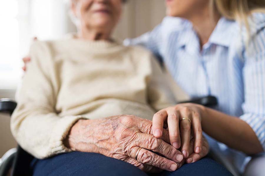 Long-Term Care Insurance - Close-up of a Senior Woman in a Wheelchair with a Focus on Her Hands Sitting with a Health Care Worker at a Senior Care Facility